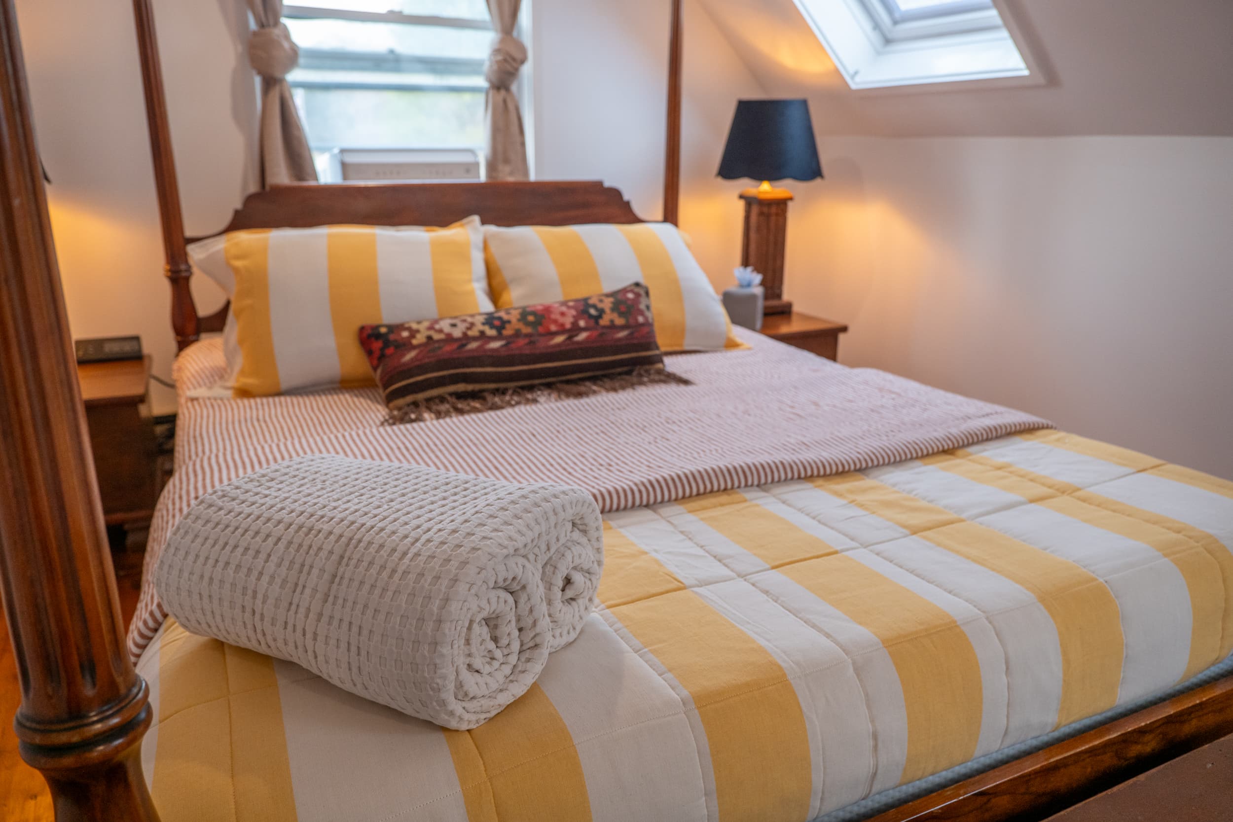 Four-poster bed with striped bedding and kilim pillow