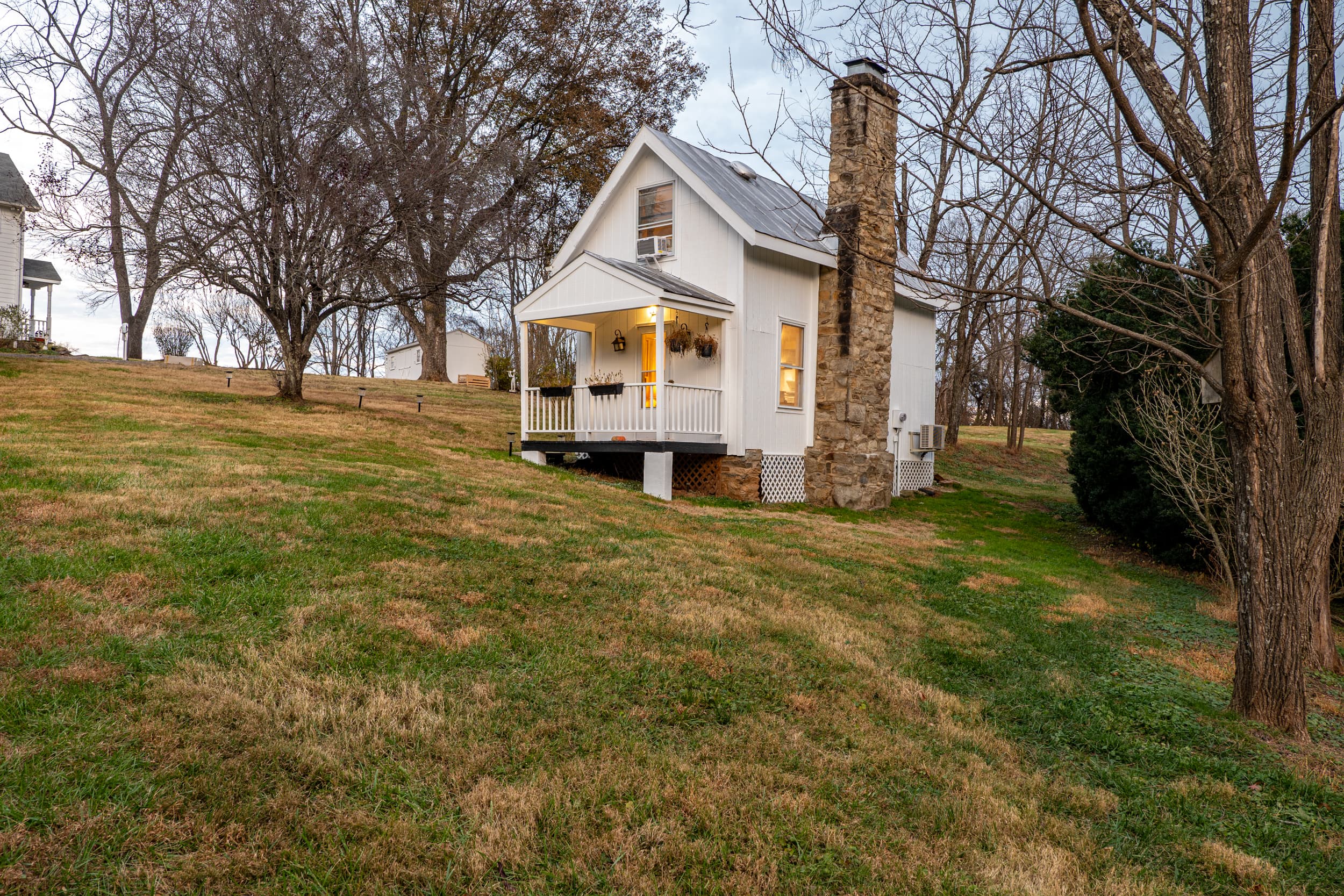 The tiny home at Ingleside Farm, a white cottage with stone chimney on a gentle hillside
